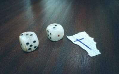 Well-worn dice sit on a table adding up to five. A scrap of paper with a scibbled blue in cross sits beside them.
