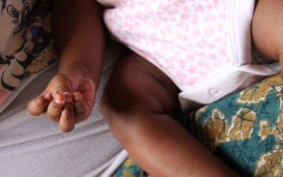 A close up of a baby's hand and legs a she lays resting on a bed