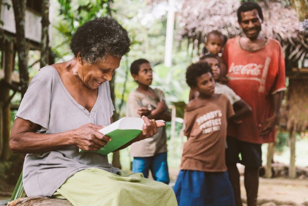 Papua New Guinean Woman Reading the Bible in her language with her family standing behind her.